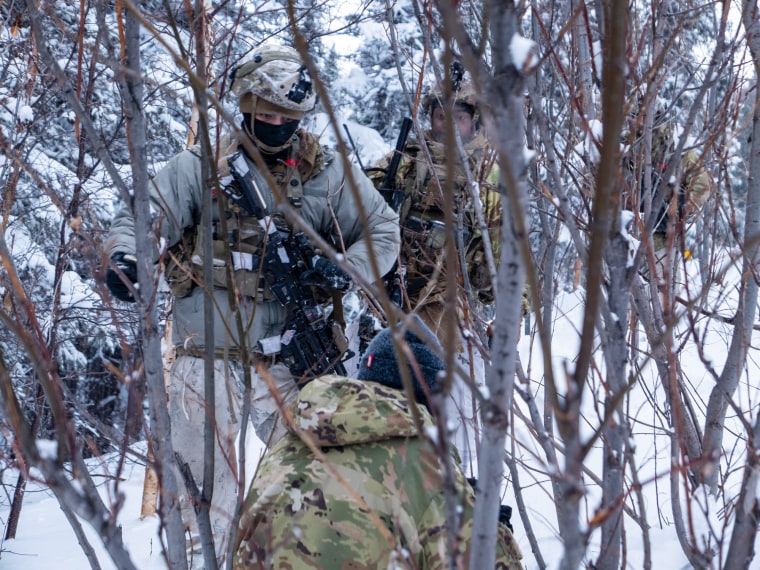 Dois soldados caminham por entre as árvores na neve enquanto um cinegrafista os filma