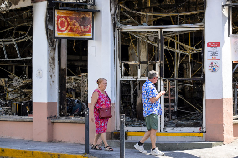 Two people walk past a burnt building
