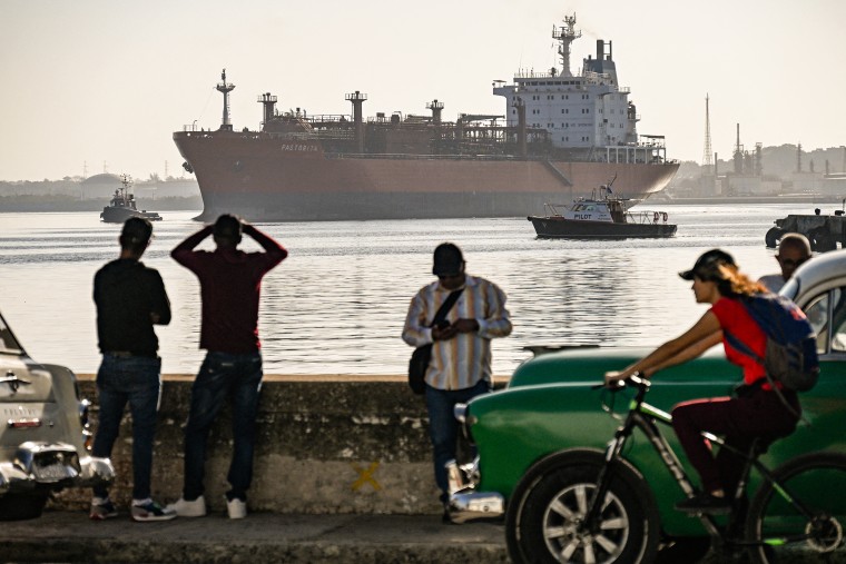 A large tanker ship looms in the distance behind a busy street view in Havana, Cuba.