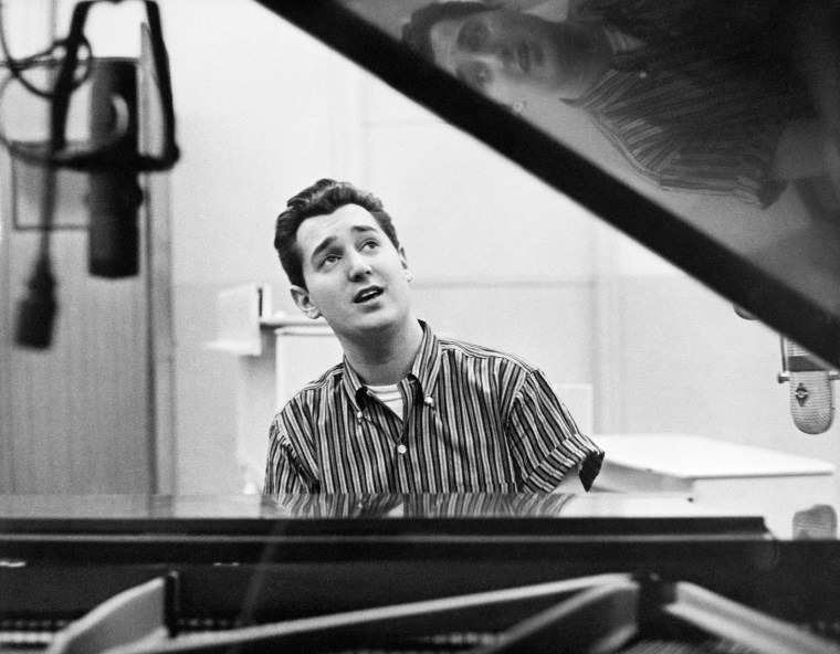 A black and white photo of the Singer Neil Sedaka Seated at a Piano.