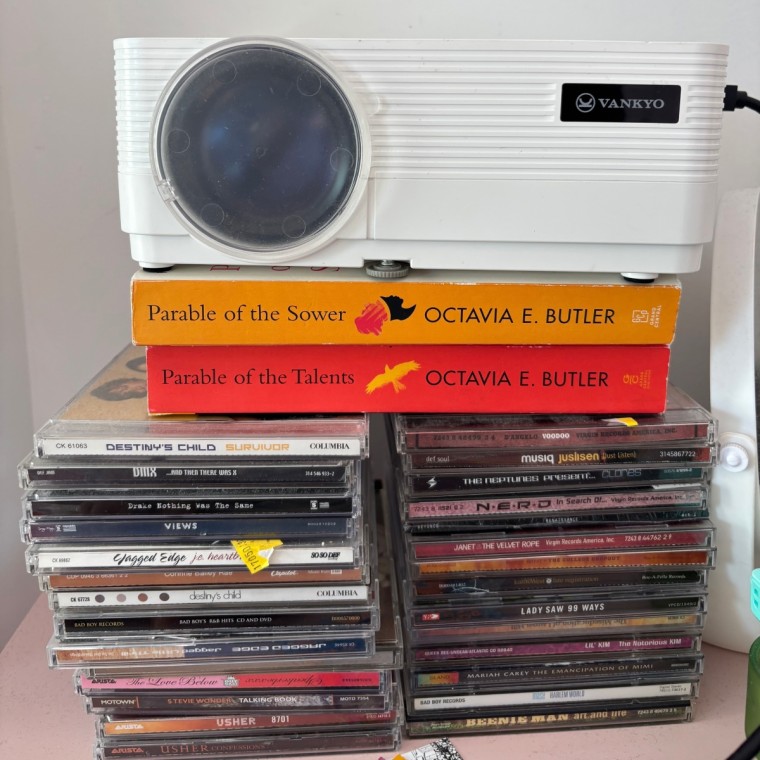 A stack of CDs underneath two books and a small bedroom projector.