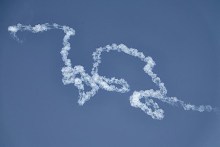 A curling line of white smoke stretches through a clear blue sky.