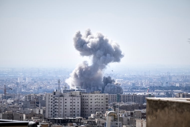 A plume of smoke rises over buildings