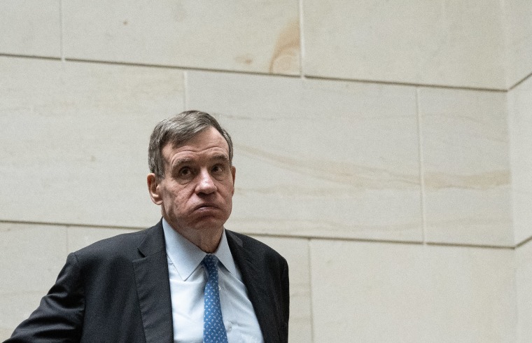 Mark Warner exhales in front of a stone interior wall at the U.S. Capitol.
