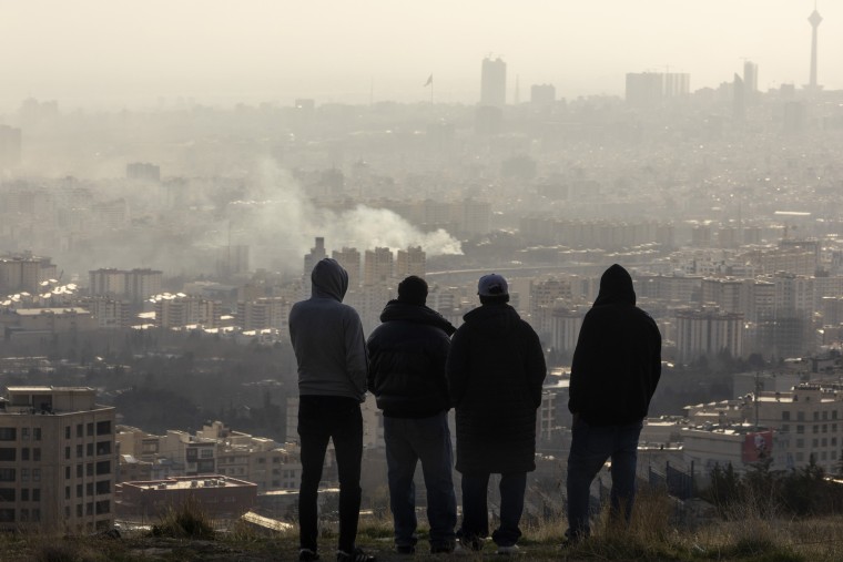 Men watch from a hillside as a plume of smoke rises after an explosion on March 2, 2026 in Tehran, Iran. 