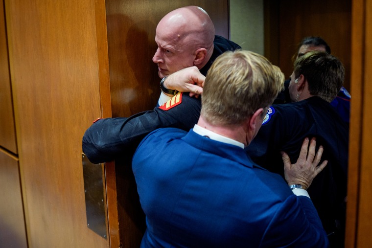 Three men pull another man wearing a military formal uniform through a wooden doorway at the U.S. Capitol