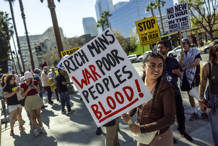 Image: A protester holds a placard reading "rich man's war poor peoples blood!"