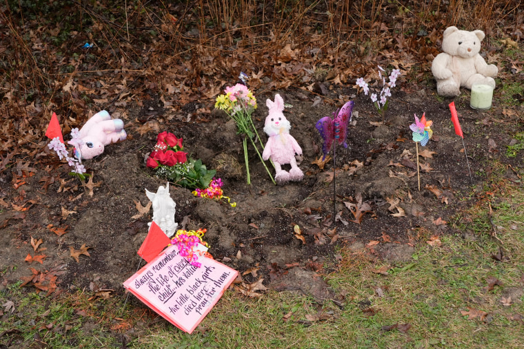 A small makeshift memorial with stuffed animals and flowers on leaf-covered ground.