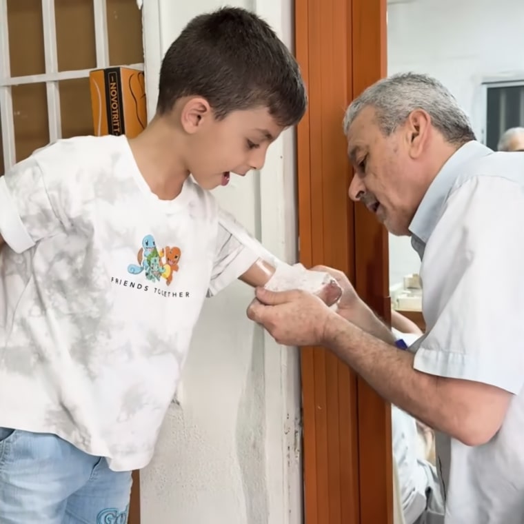 Omar's left arm, of which only half remains, is bandaged by a man