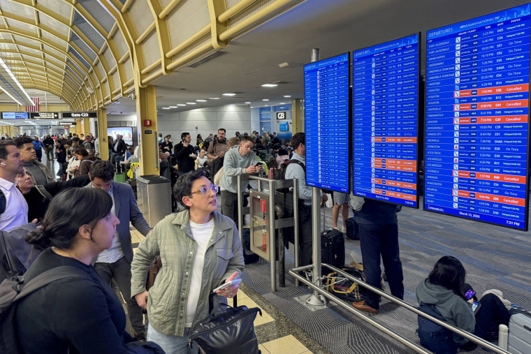Travelers look at a departures screen inside a terminal.