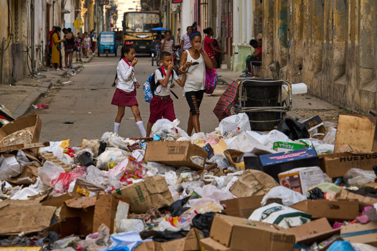 People hold their noses as they pass a street a pile of garbage in Havana on Feb. 17, 2026.