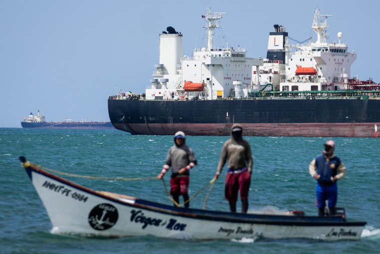 Fishermen pass an oil tanker while on a boat in the water