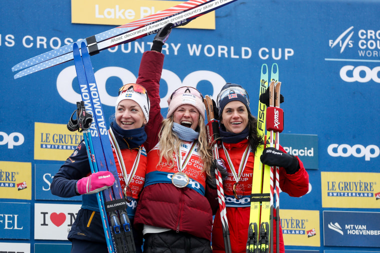 Three women skiers on the winners podium in front of a step-and-repeat backdrop. 