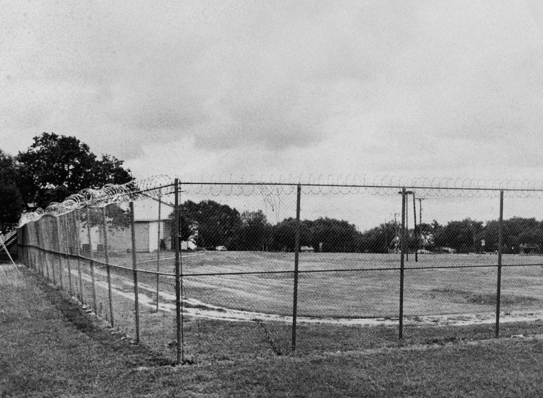 A black and white photo shows a grassy field with barbed wire fencing around it.