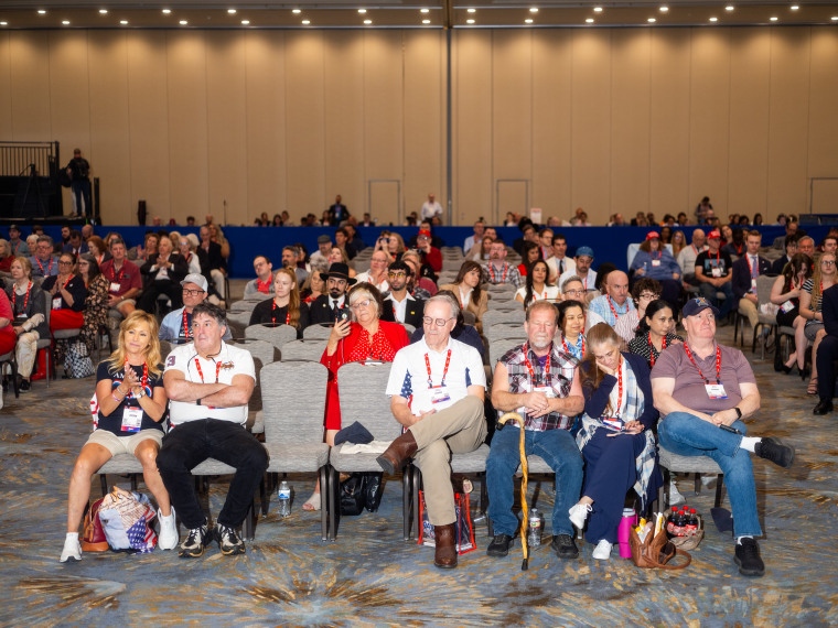 People sitting on rows of cushioned chairs inside a conference room during CPAC. 