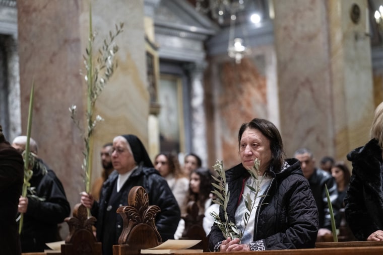 As pessoas sentam-se em bancos e seguram folhas de palmeira