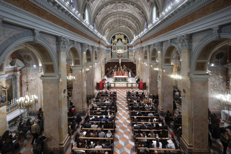 Uma visão ampla do interior de uma igreja ornamentada, com pessoas sentadas em bancos e altares