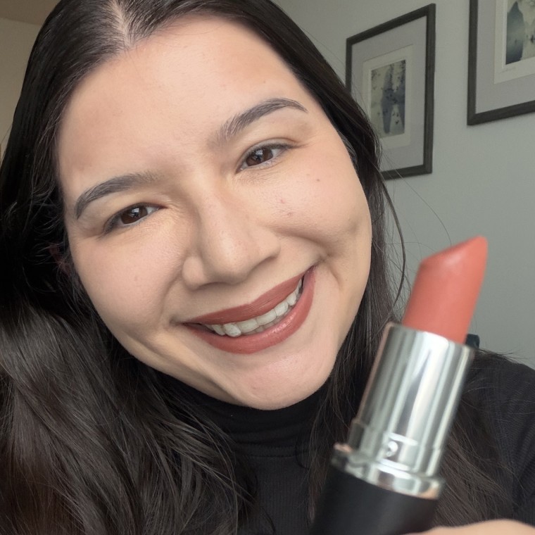 An editor smiles while wearing the MAC lipstick shade Taupe and holds the lipstick up to the camera.