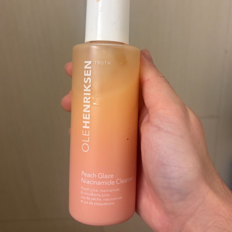 Women in bathroom holding up the Olehenriksen Peach Glaze 2% Niacinamide Cleanser.