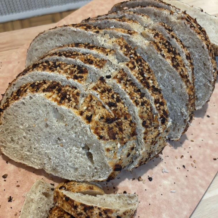 A loaf of Wildgrain's Gluten-Free Sourdough Everything Loaf on a cutting board with some pieces sliced.