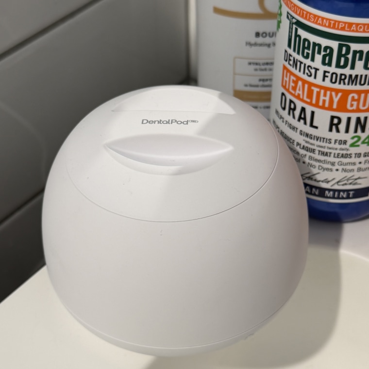 White Zima Dental Pod on a bathroom counter with Therabreath and Billie lotion seen in the background behind it.