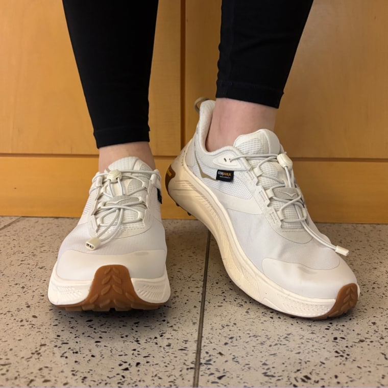 A person wearing white Hoka Transport 2 sneakers outside.