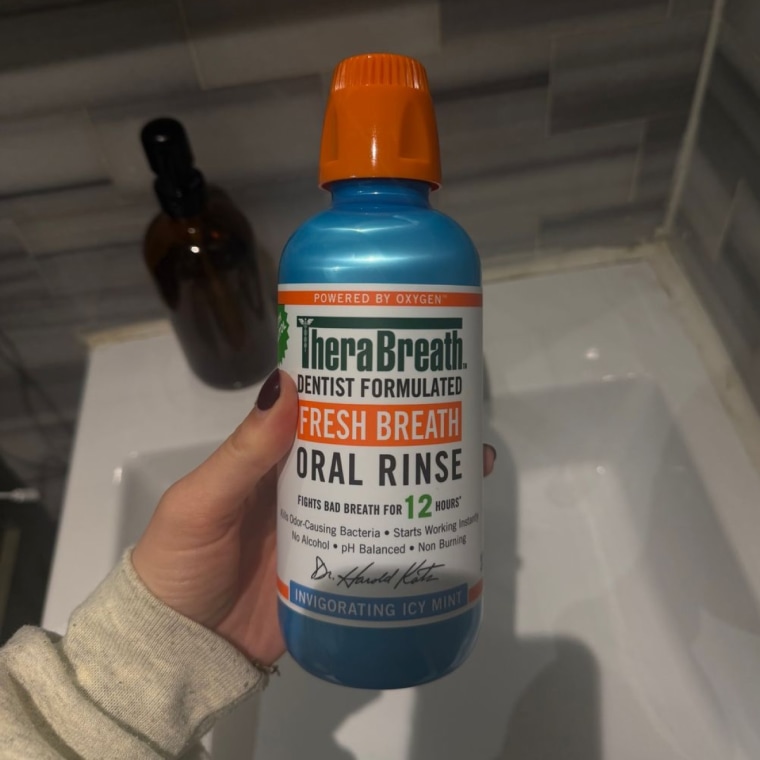 Hand holding a blue bottle of Therabreath mouthwash.