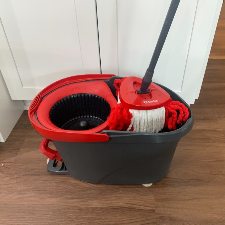 O-Cedar mop bucket sitting on tile floor with mop handle inside.
