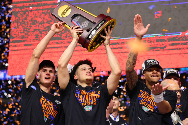 Walter Clayton holds a trophy over his head while flanked by two teammates.