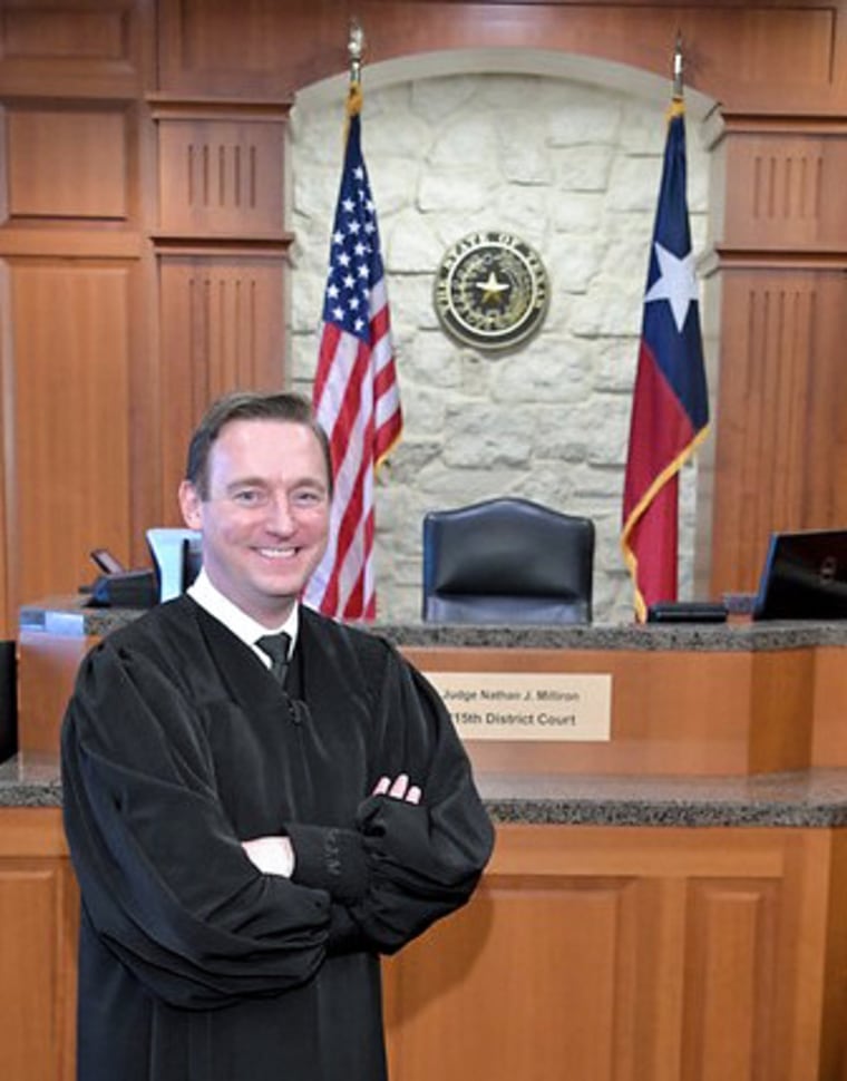 Nathan J. Milliron stands inside of a courtroom by the judge's seat wearing a judge's robe
