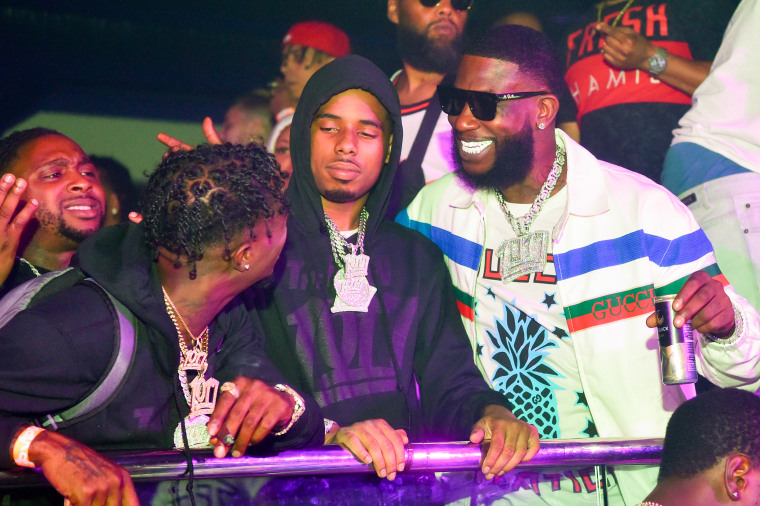Gucci Mane and other rappers appear inside a nightclub under colored lights.