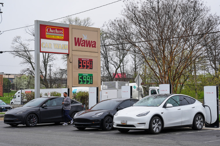 Electric vehicles charge as the price of fuel is displayed at a gas station
