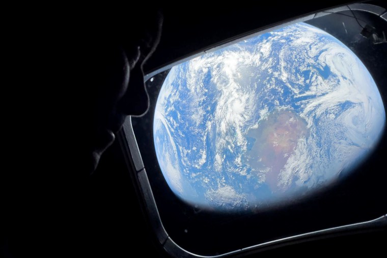 Imagem: Close de um astronauta olhando pela janela de uma espaçonave com vista para a Terra