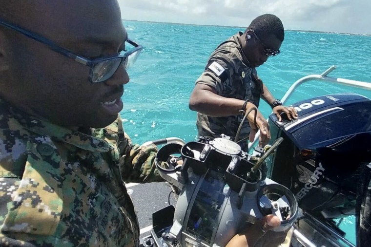Two men wearing camouflage fatigues aboard a small boat. 