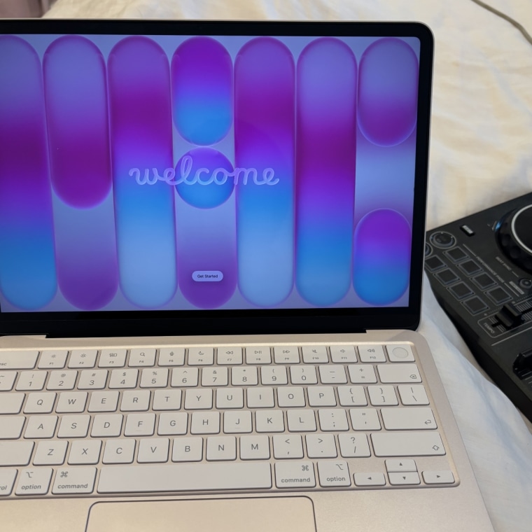 The Macbook Neo hooked up to the Pioneer DDJ on a pink bedspread.