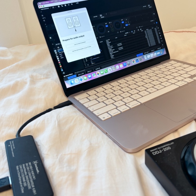 The adapter connected to a pink Macbook Neo on a pink bedspread.
