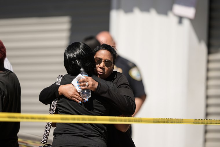 امرأتان تتعانقان خلف شريط الشرطة الأصفر في مسرح الجريمة.