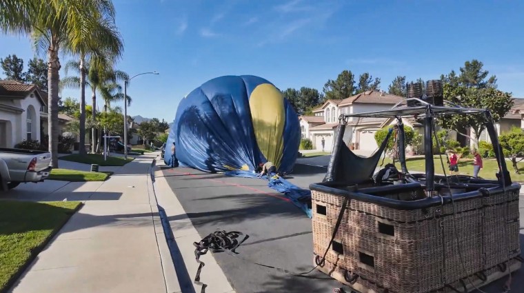 A hot air balloon is deflated in the middle of a street between houses