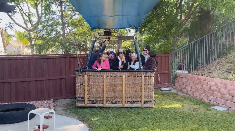 A hot air balloon with several people inside sat in a backyard