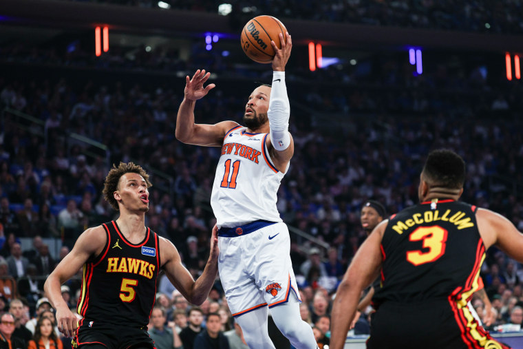 Jalen Brunson salta para fazer uma cesta entre dois outros jogadores