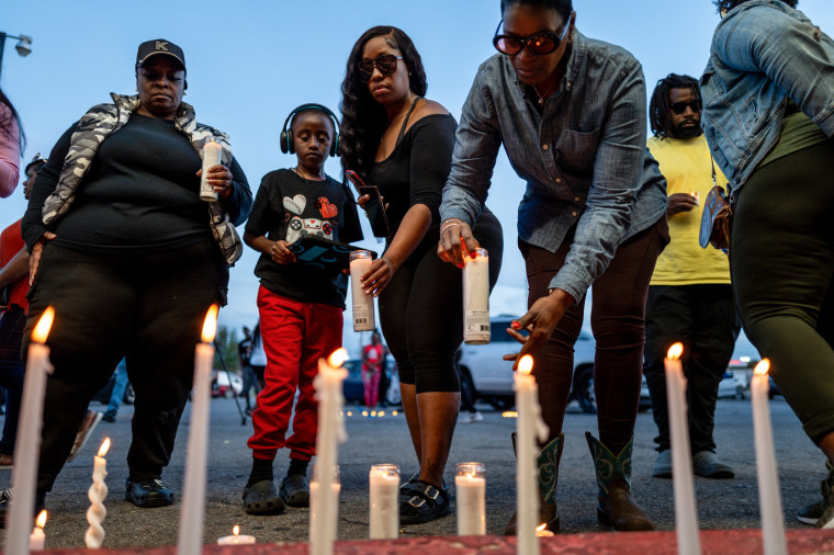 People stand in front of candles lit on the ground outside