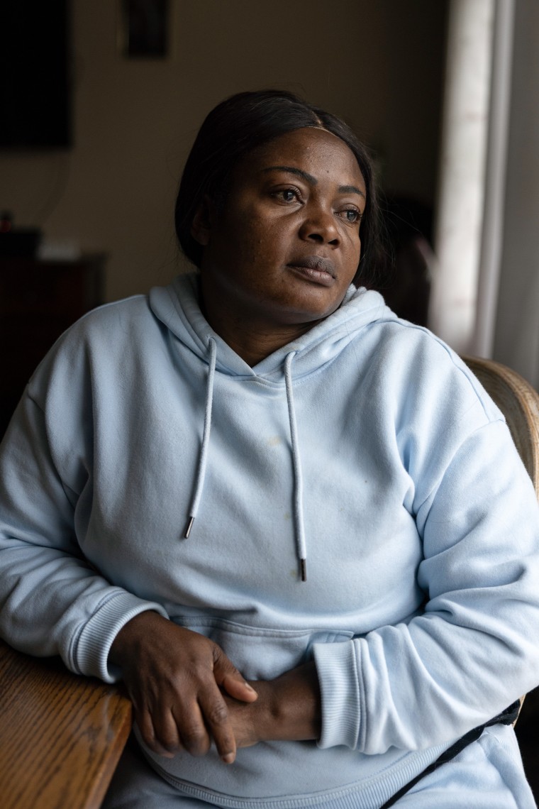 A woman in a light blue hooded sweatshirt gazes out a window while seated at a wooden table.