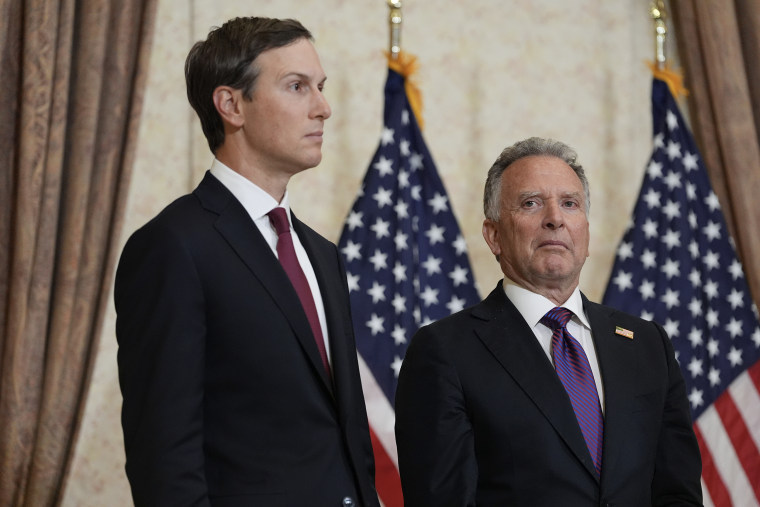 Jared Kushner and Steve Witkoff stand in front of two American flags.