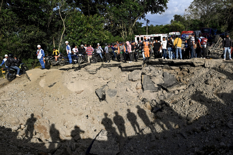 A large group of people surround a crater in the middle of a highway after a bombing attack.