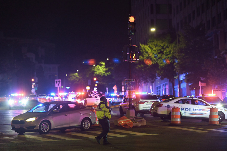 Red and blue lights atop law enforcement vehicles illuminate a city streetscape at night.