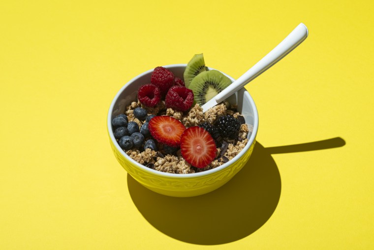 Bowl with muesli, chocolate, and fruits on yellow background