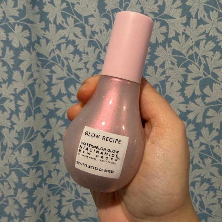 Hand holding the Glow Recipe Watermelon Glow Niacinamide Dew Drops against blue and white flowered wallpaper.