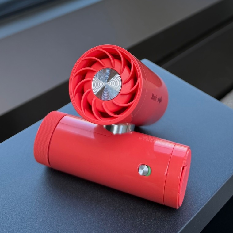 Red mini fan on a table with the city in the background.