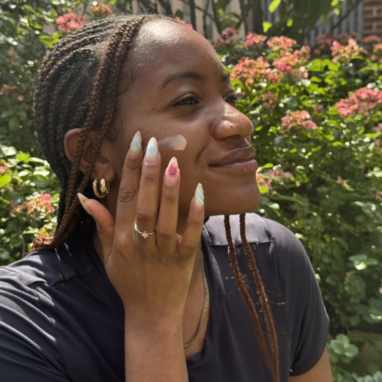 A woman applying Tatcha’s The Silk Sunscreen on her cheek while outside.