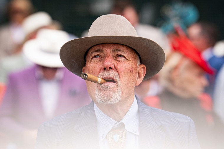 A man smokes a cigar while watching the fourth race.